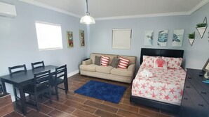 Un dormitorio con cama, sofá, mesa de comedor con sillas, televisor y obras de arte en las paredes.