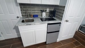 Una cocina compacta con armarios blancos, un lavamanos de acero inoxidable, una estufa integrada y un microondas.