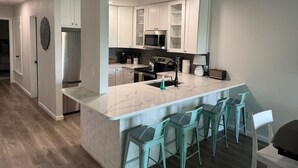 A modern kitchen with white cabinets, a central island with bar stools, and a stainless steel refrigerator. - Lake Travis townhome-Pool-Marina-Boat ramp-Golf (Point Venture)
