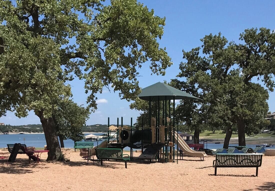 A playground with a slide, swings, and a covered play area, surrounded by trees and benches.