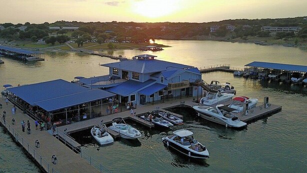 A waterfront dock with boats, a covered seating area, and a building with a blue roof. - Lake Travis townhome-Pool-Marina-Boat ramp-Golf (Point Venture)