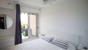 A bedroom with a bed, a ceiling fan, a window with curtains, a bedside table, and a nightstand. - Modern apartment, 2 bedrooms, sea view terrace, (LA SEYNE SUR MER)