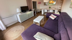 A modern living room with a sofa, a TV, a dining area, and a kitchen. - Modern apartment, 2 bedrooms, sea view terrace, (LA SEYNE SUR MER)