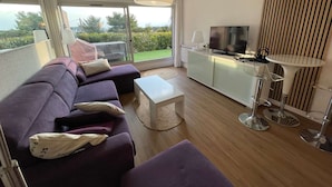A modern living room with a sofa, a coffee table, a TV, and a balcony with a view. - Modern apartment, 2 bedrooms, sea view terrace, (LA SEYNE SUR MER)