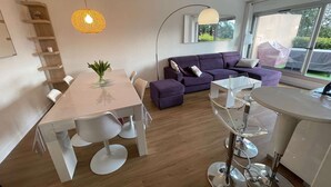 A modern living room with a dining area, a purple sofa, and a large window providing a view of the outdoors. - Modern apartment, 2 bedrooms, sea view terrace, (LA SEYNE SUR MER)