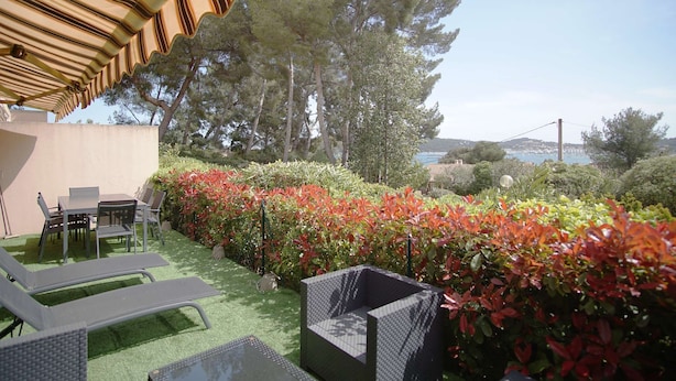 A patio with a table and chairs, surrounded by green artificial turf and red foliage. - Modern apartment, 2 bedrooms, sea view terrace, (LA SEYNE SUR MER)