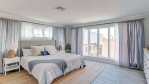 A bedroom with a large bed, a nightstand, a dresser, and a window with curtains.