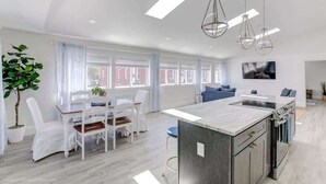 A modern kitchen with a central island, white dining chairs, and a large window with curtains.