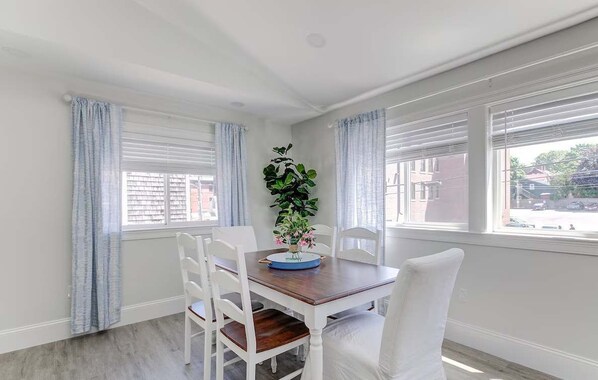 Un comedor con una mesa de madera, sillas blancas y una planta en maceta.