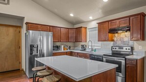A modern kitchen with a large island, stainless steel appliances, wooden cabinets, and a tiled backsplash. - Happy Valley Home, Game Room, & 8 beds! (Happy Valley)