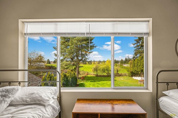 A bedroom with a large window, two beds, and a small wooden table. - Happy Valley Home, Game Room, & 8 beds! (Happy Valley)