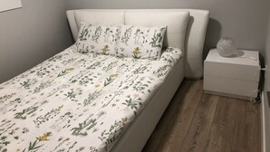 A bedroom with a bed, floral bedding, a bedside table with a lamp, and a wooden floor. - A - Modern Cozy Room w Private Entrance & Washroom (Surrey)