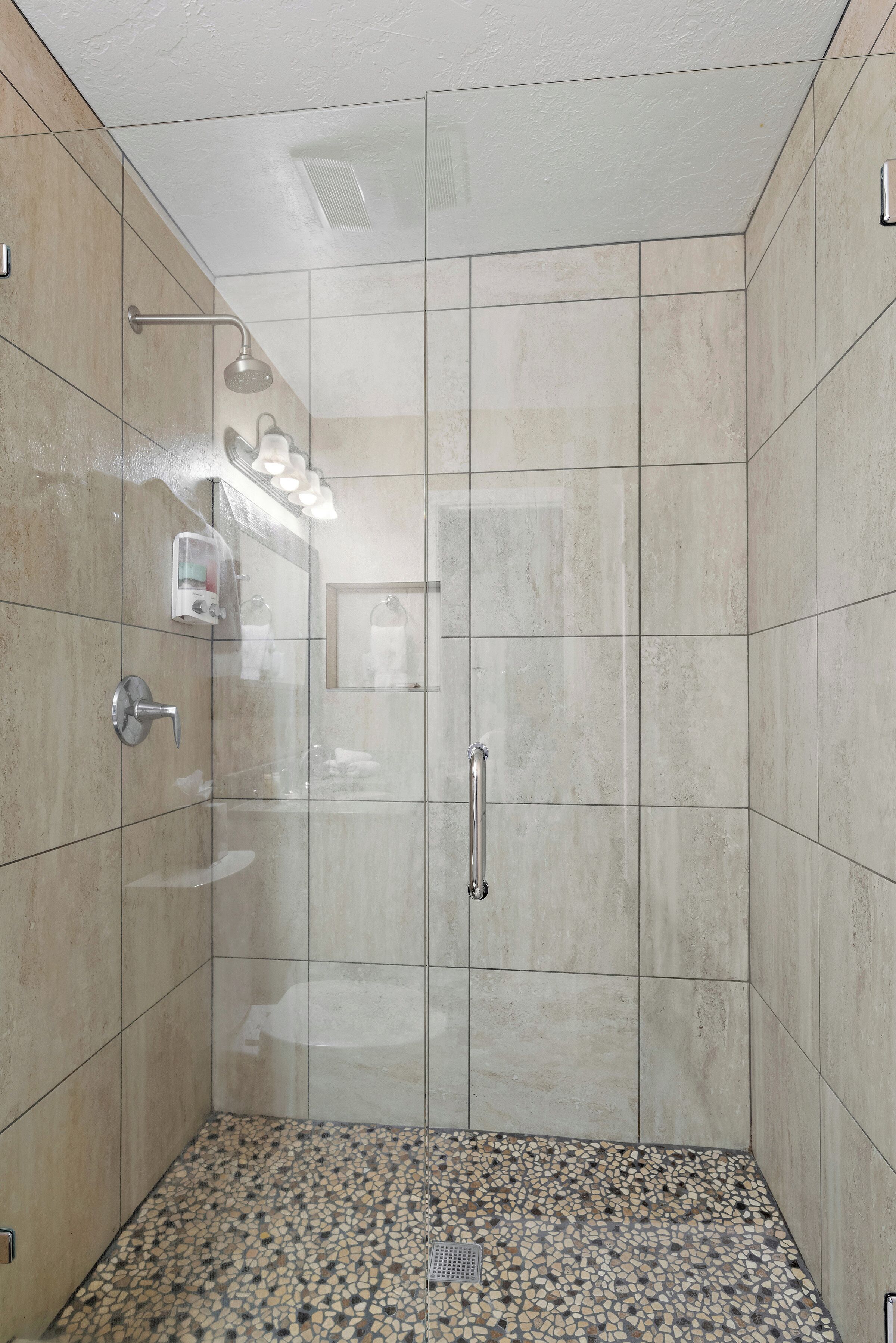 Une douche à l’italienne avec un sol carrelé, une porte en verre et une barre d’appui.