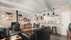 A living room with a black leather sofa, a wooden coffee table, and a fireplace. There is a kitchen area with white cabinets and a stove. - Fort Marcy 32 | Walk to Plaza | Fireplace | Kitchen | Hot Tub | Pool | End Unit | Single Level (Santa Fe)