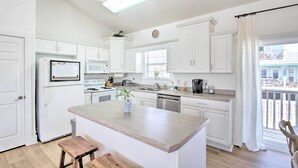 A modern kitchen with white cabinets, a central island, and a view of the balcony. - Pensacola Beach Home: 1 Block to Beach Access (Pensacola Beach)