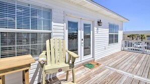 A wooden deck with a chair and table, a white house with large windows and a door, and a clear blue sky. - Pensacola Beach Home: 1 Block to Beach Access (Pensacola Beach)