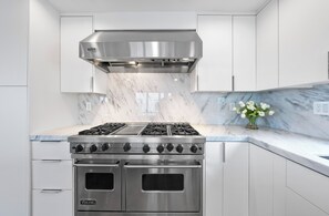 A kitchen with a stainless steel Viking stove, white cabinets, and a marble backsplash.