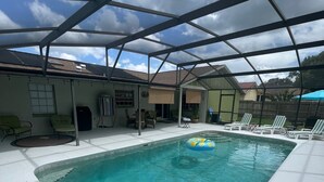 A covered swimming pool with a clear blue water, surrounded by lounge chairs and a patio area.