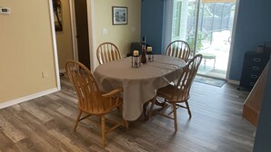 A dining area with a round table, six wooden chairs, a ceiling fan, and a view through a sliding glass door to an outdoor patio.
