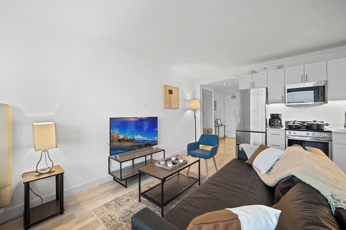 Una sala de estar moderna con una televisión de pantalla plana, un sofá, una mesa de centro y una cocina con microondas y estufa.