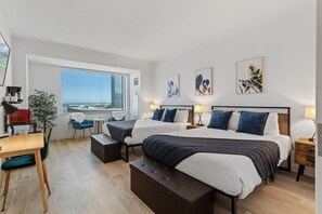 A hotel room with two beds, a desk, a chair, a small table, and a large window with a view. - CozySuites at Showboat (Atlantic City)