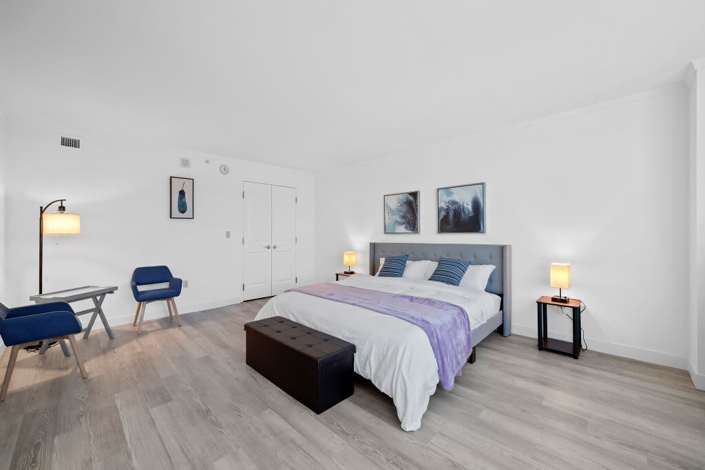 A modern bedroom with a bed, two chairs, a table, a bench, and two bedside lamps.