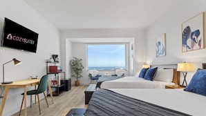 Moderni hotellihuone, jossa on suuri sänky, työpöytä, tuoli, televisio ja näköala merelle.