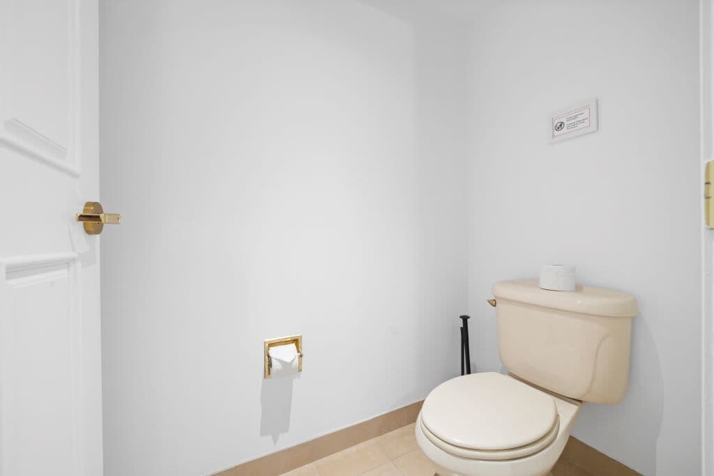 Une petite salle de bain propre, équipée de toilettes, d’un distributeur de serviettes et d’un porte-rouleau de papier toilette fixé au mur.