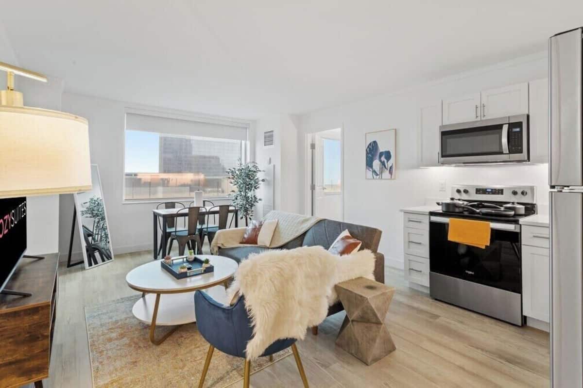A modern apartment with a living room, dining area, and kitchen. It includes a sofa, a dining table, a TV, and a kitchen with a stove and microwave.