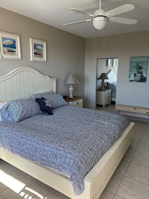 A bedroom with a bed, a ceiling fan, a nightstand, a lamp, and two framed pictures on the wall. - Penthouse Condo with Ocean View in the Heart of Siesta Key (Sarasota)