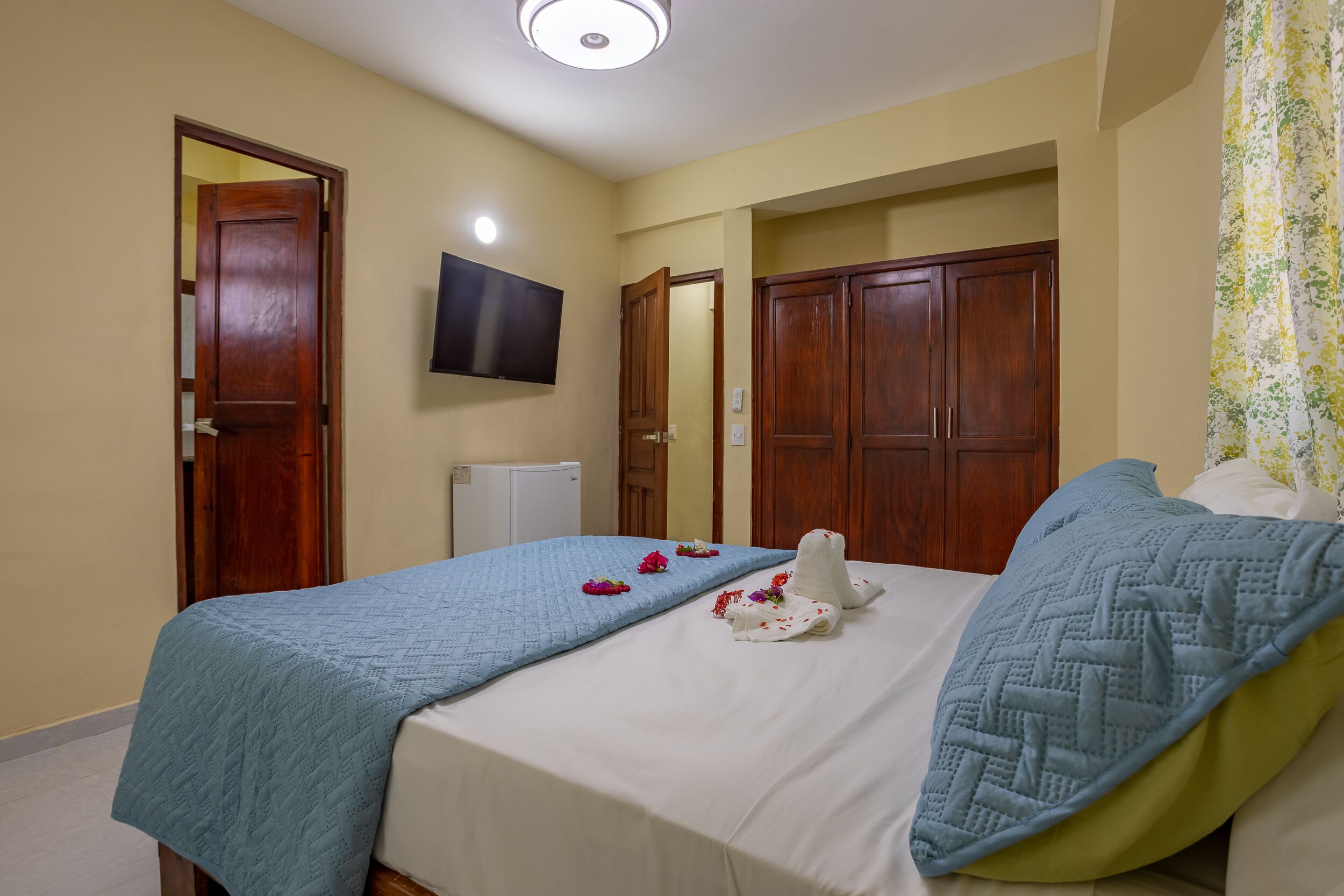 A hotel room with two beds, a flat-screen TV, wooden wardrobes, and a ceiling light.