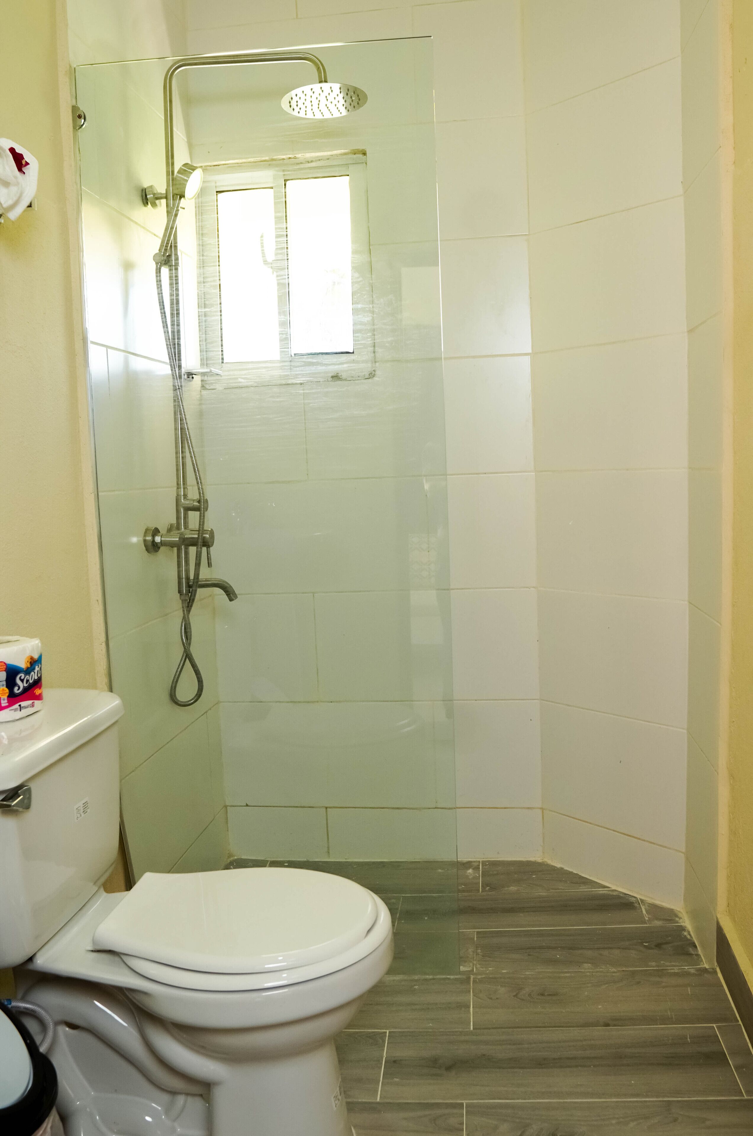 Une salle de bain avec une douche à parois de verre, des toilettes et une petite fenêtre.