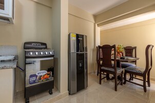 Cocina compacta con estufa a gas, horno y refrigerador de acero inoxidable. Hay una mesa de comedor con cuatro sillas y una planta en maceta sobre la mesa.