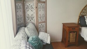 Un dormitorio con una cama, cabecera de madera, mesita de mimbre y alfombra blanca y mullida.