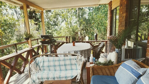 Un espacio de estar al aire libre techado con muebles de madera, una mesa y plantas en macetas.