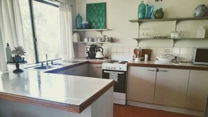 Una cocina con una isla central, estufa, fregadero y microondas. Hay estantes sobre la estufa con varios objetos.
