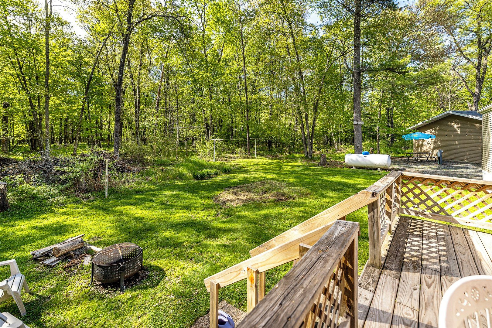 A deck with a wooden railing, a picnic table, and a small shed in a wooded area.