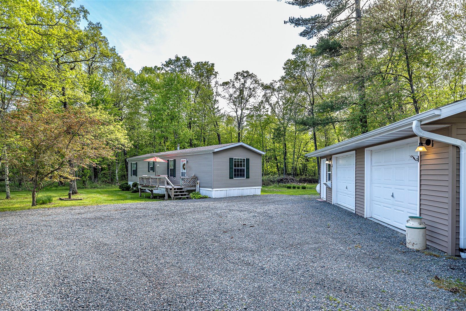 A single-story cabin with a gravel driveway, a front deck, and a garage.