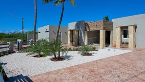 A modern building with a courtyard, palm trees, and a clear blue sky. - Beautiful fully gated private home with resort like amenities (Noord)