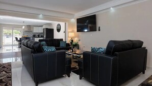 A modern living room with black leather sofas, a flat-screen TV, and a dining area with a table and chairs. - Beautiful fully gated private home with resort like amenities (Noord)