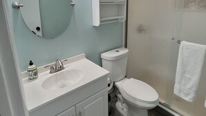 A bathroom with a white vanity, a round mirror, a toilet, and a glass shower enclosure.