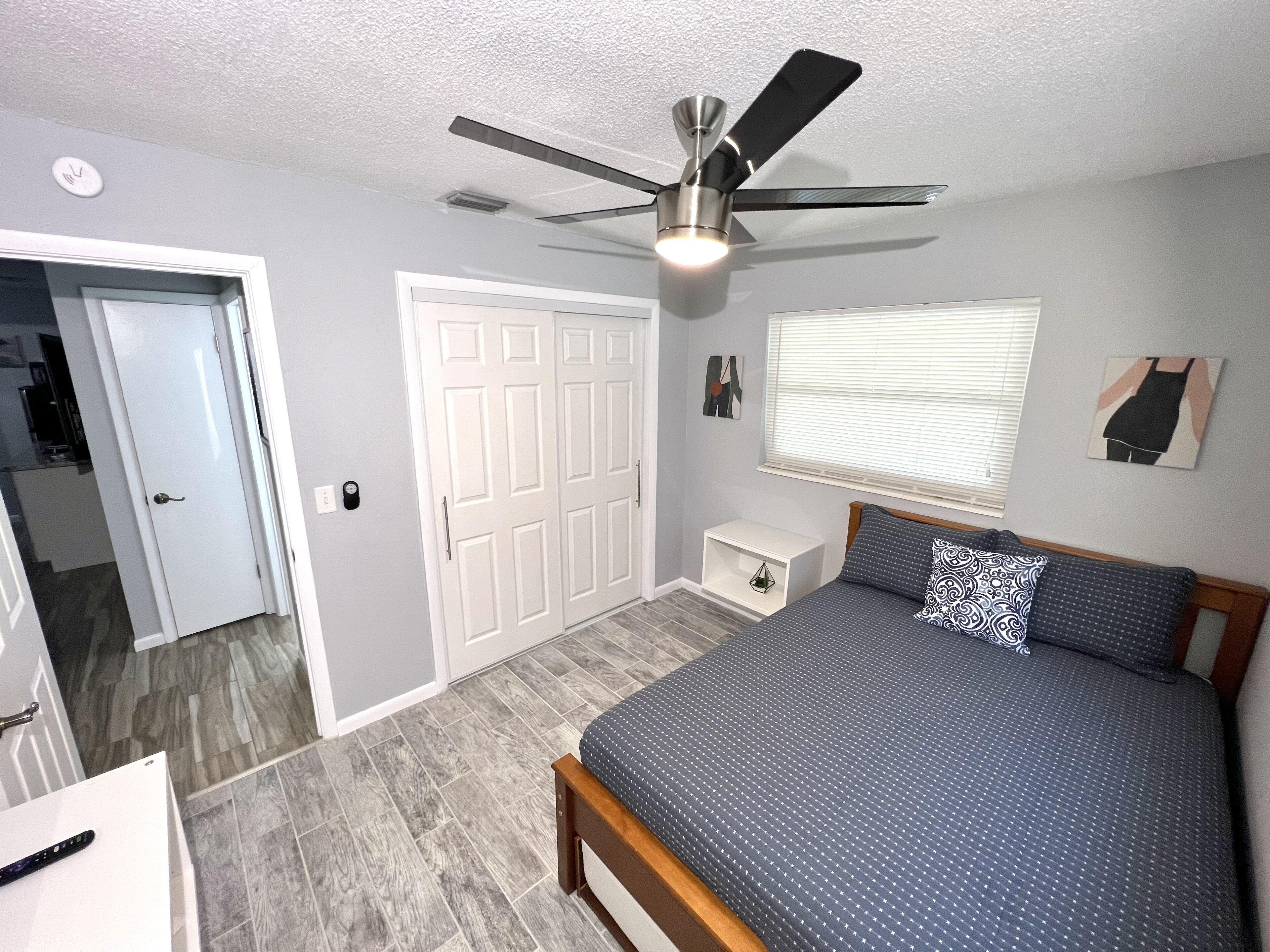 A bedroom with a bed, a ceiling fan, a nightstand, a wardrobe, and a window with blinds.