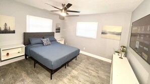 A bedroom with a bed, a ceiling fan, a nightstand, a dresser, and a window with blinds.