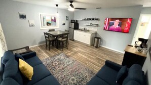 A compact living space with a sofa set, a dining table, a kitchen area, and a TV mounted on the wall.