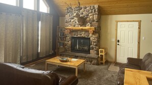 A cozy living room with a stone fireplace, wooden ceiling, and a leather couch.