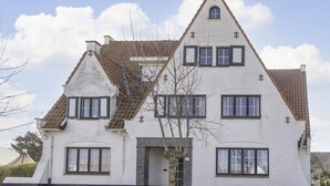 Ein zweistöckiges, weißes Gebäude mit einem steilen Dach, zahlreichen Fenstern und einem Ziegelportal.