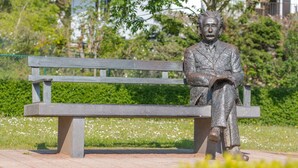 Eine Statue eines sitzenden Mannes auf einer Parkbank.