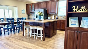 Une cuisine spacieuse avec des meubles en bois, un îlot central doté de tabourets et un coin repas avec des chaises bleues.