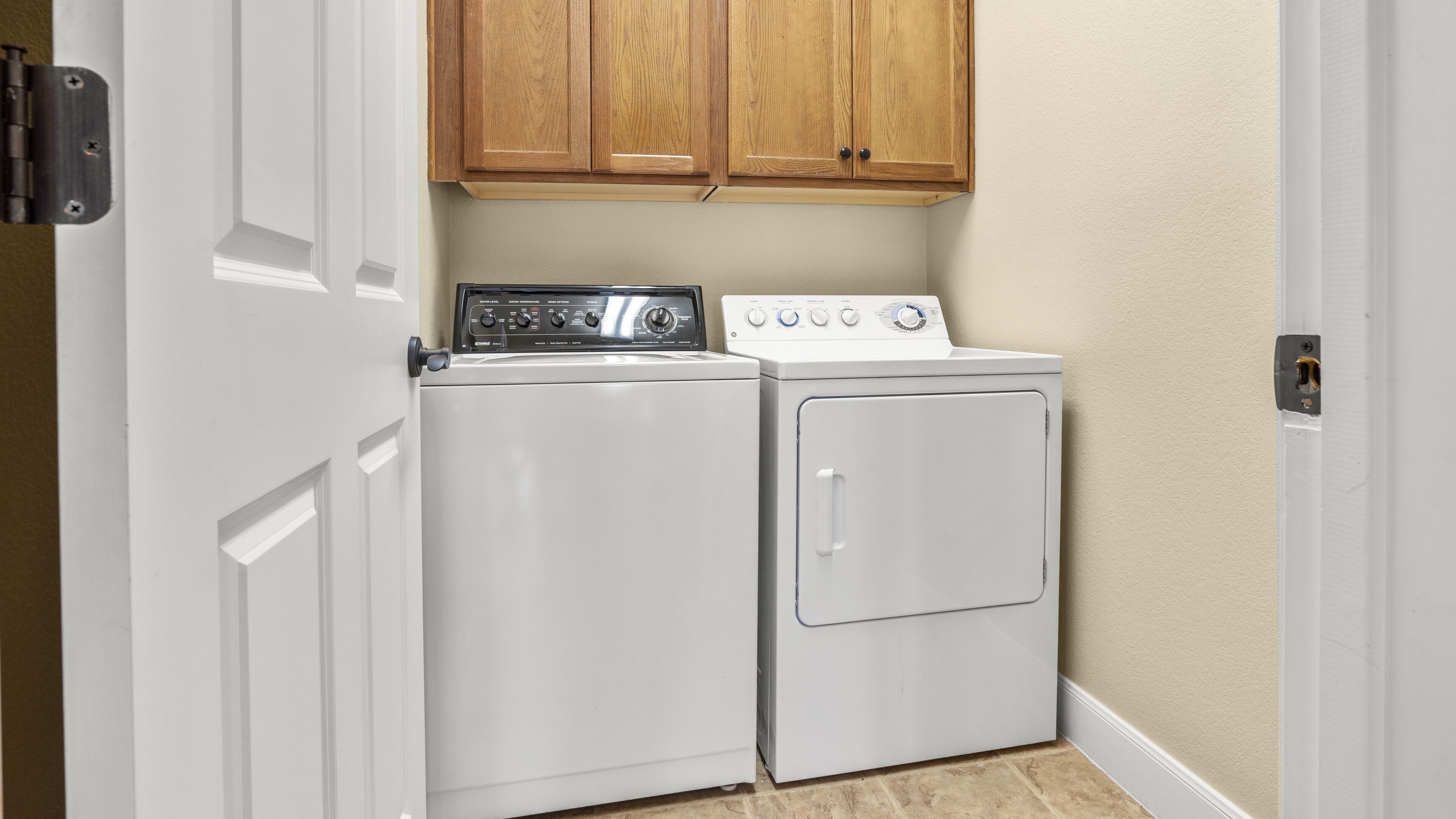Un espace buanderie équipé d’un lave-linge et d’un sèche-linge, avec des armoires en bois au-dessus et une porte blanche.