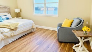 Une chambre à coucher comprenant un lit, une chaise, une table de chevet, une lampe et une fenêtre donnant sur un beau paysage.
